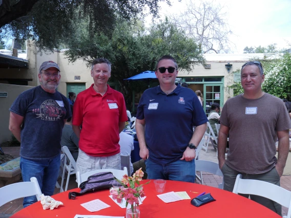 4 event attendees stand behind a table with a red cloth