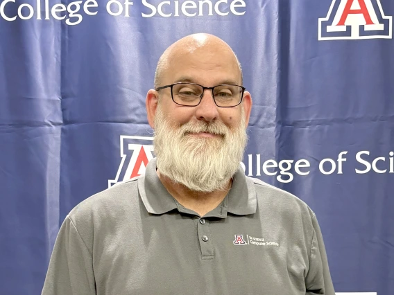 Eric Collins stands in front of a College of Science logo displaying his Excellence Award certificate