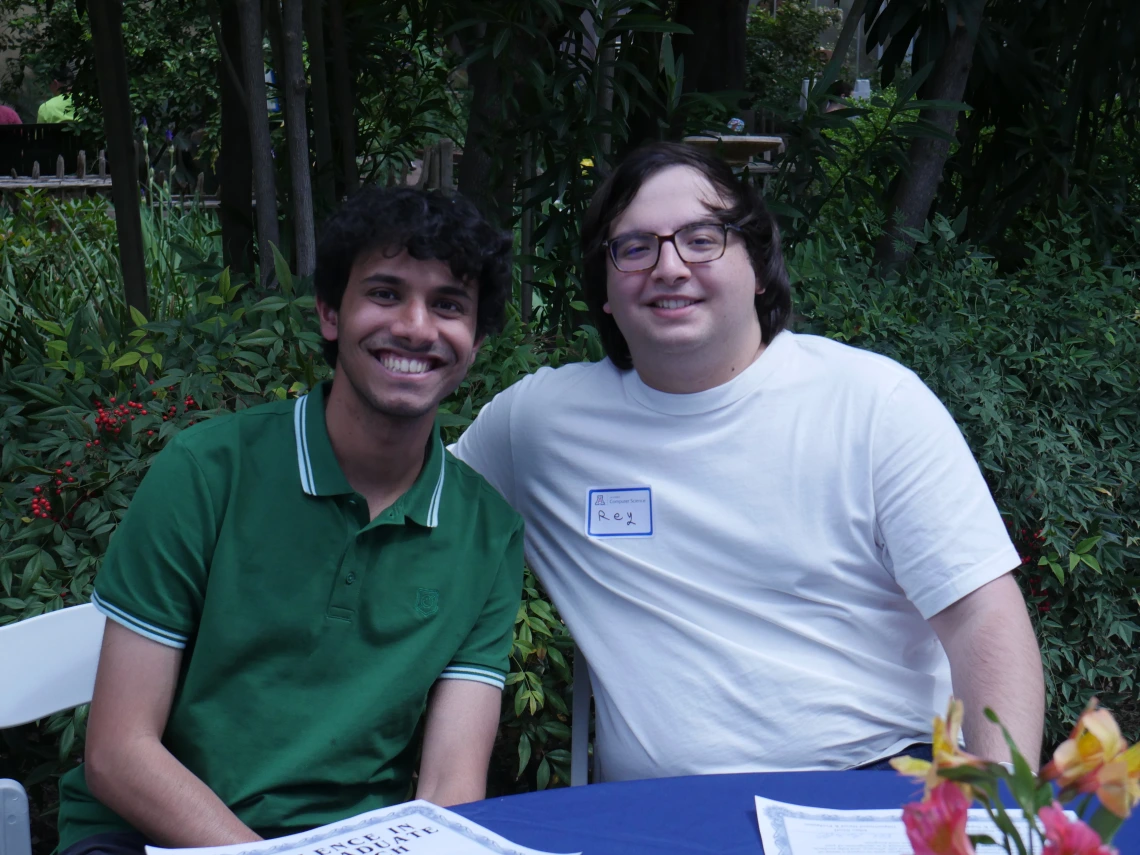 2 event attendees at a table in front of greenery