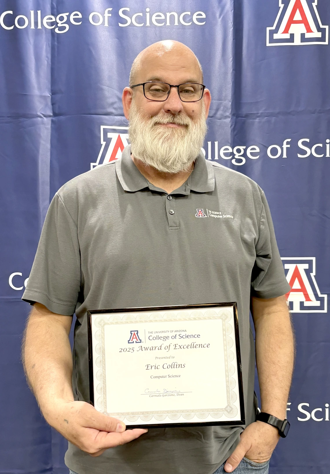 Eric Collins stands in front of a College of Science logo displaying his Excellence Award certificate